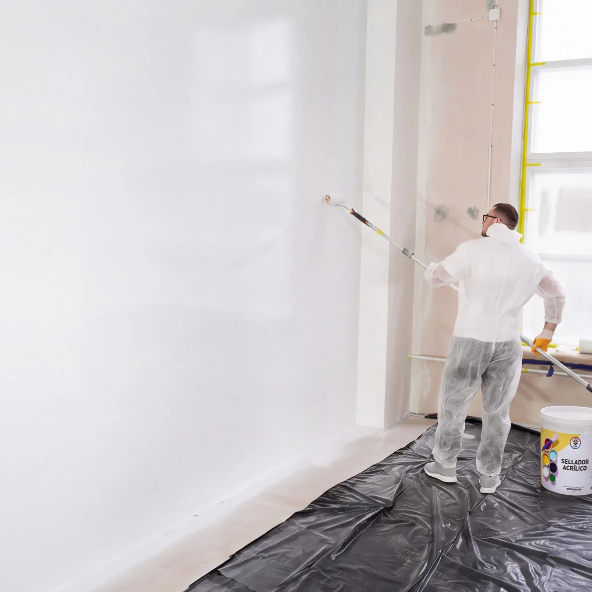 Pintor aplicando pintura con rodillo en un muro interior